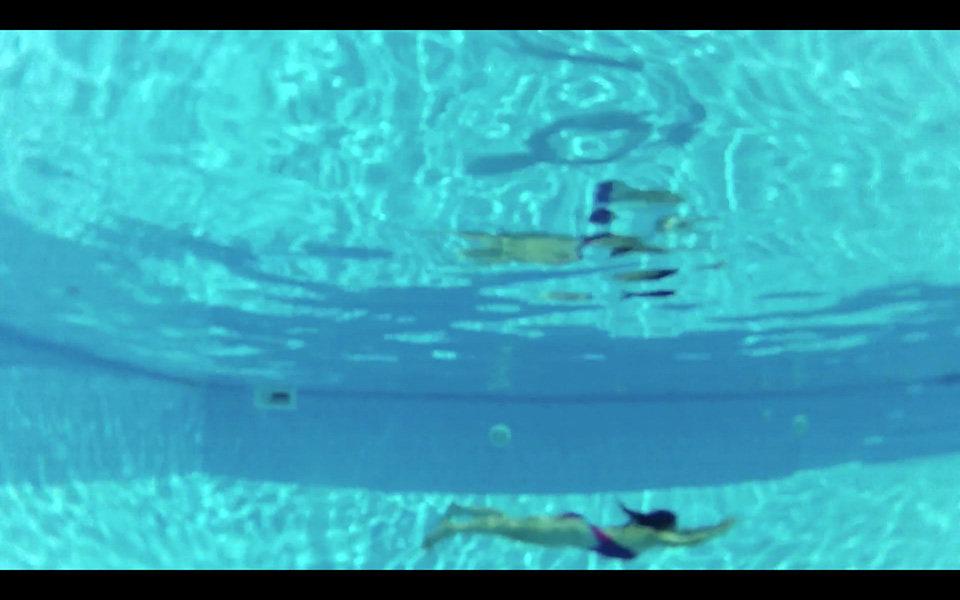 Woman swimming underwater in a pool, reflecting on the surface.